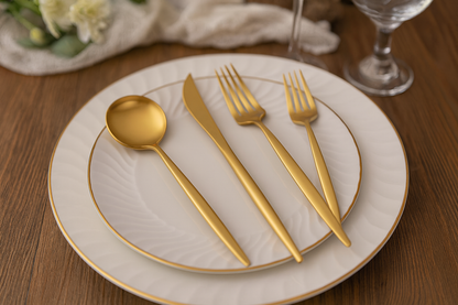 Gold stainless steel cutlery set arranged on white ceramic plates placed on a wooden dining table.