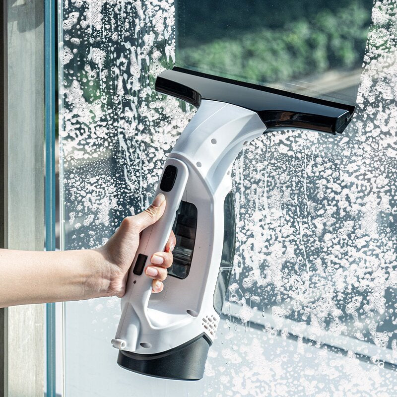 Hand using the Evivoramx Multifunctional Electric Cordless Window Cleaner Machine to remove soap and clean a glass window.